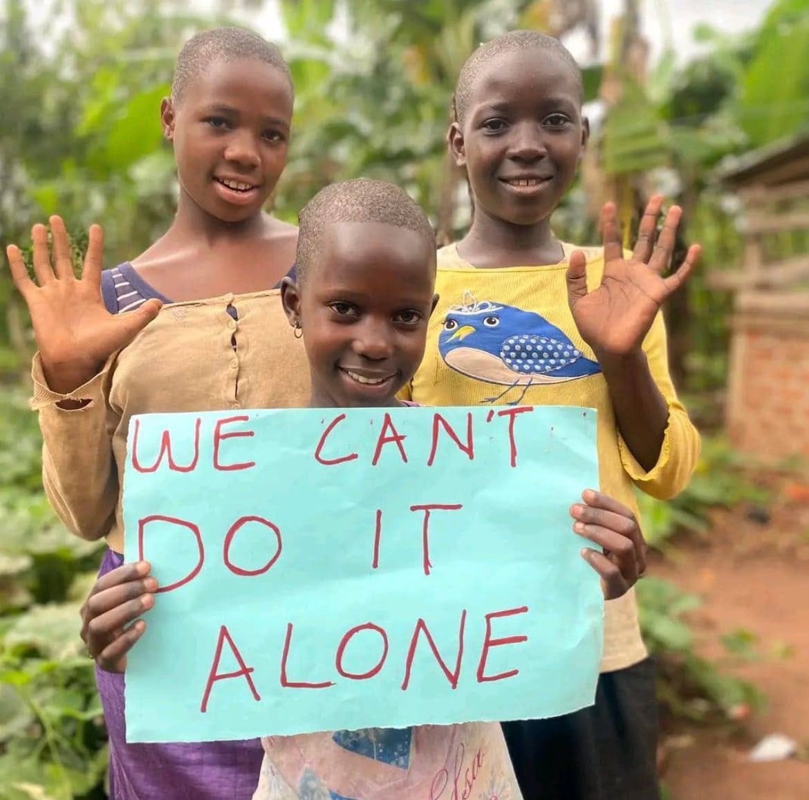 Three children holding a sign that reads: We can't do it alone