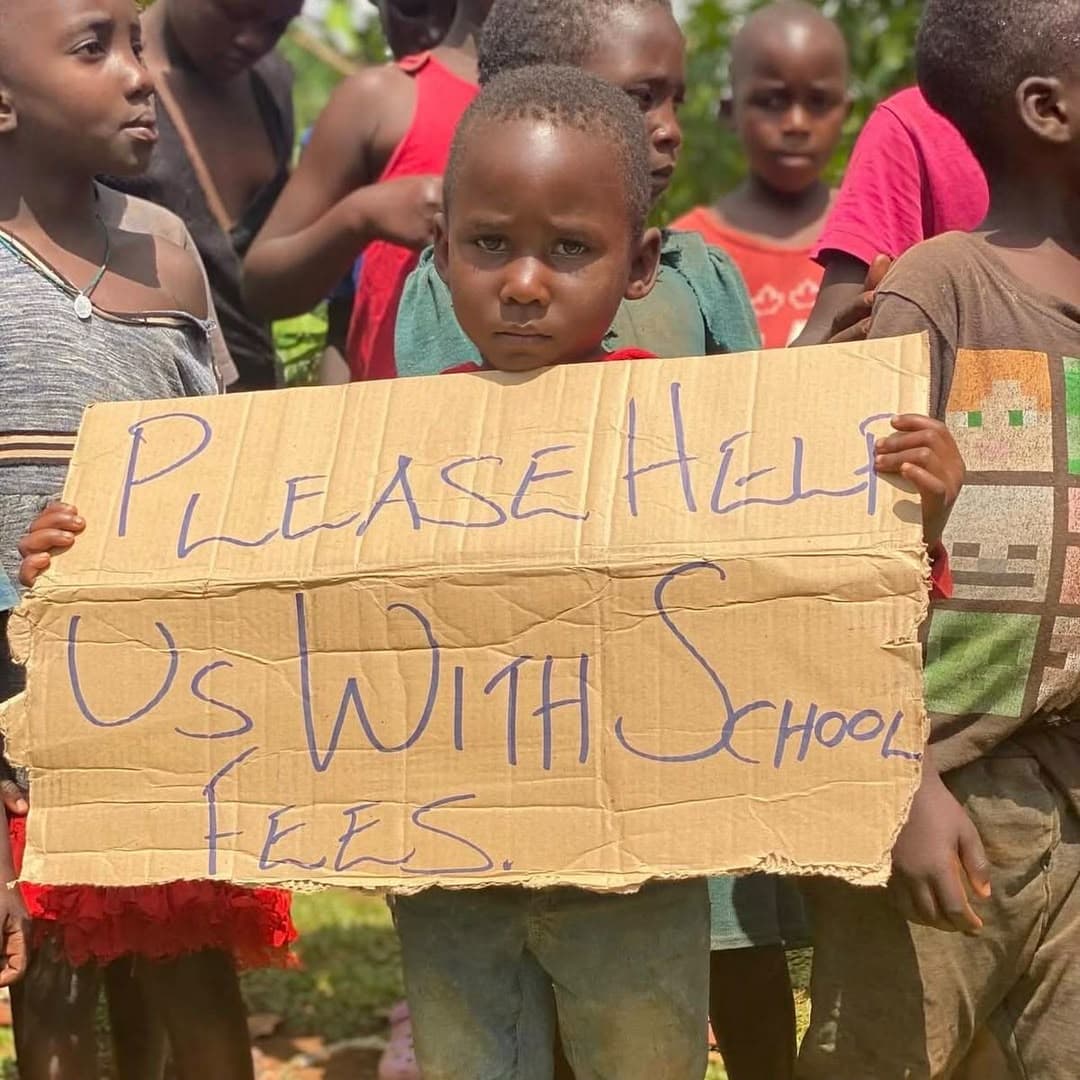 A child holding a cardboard sign asking for help with school fees